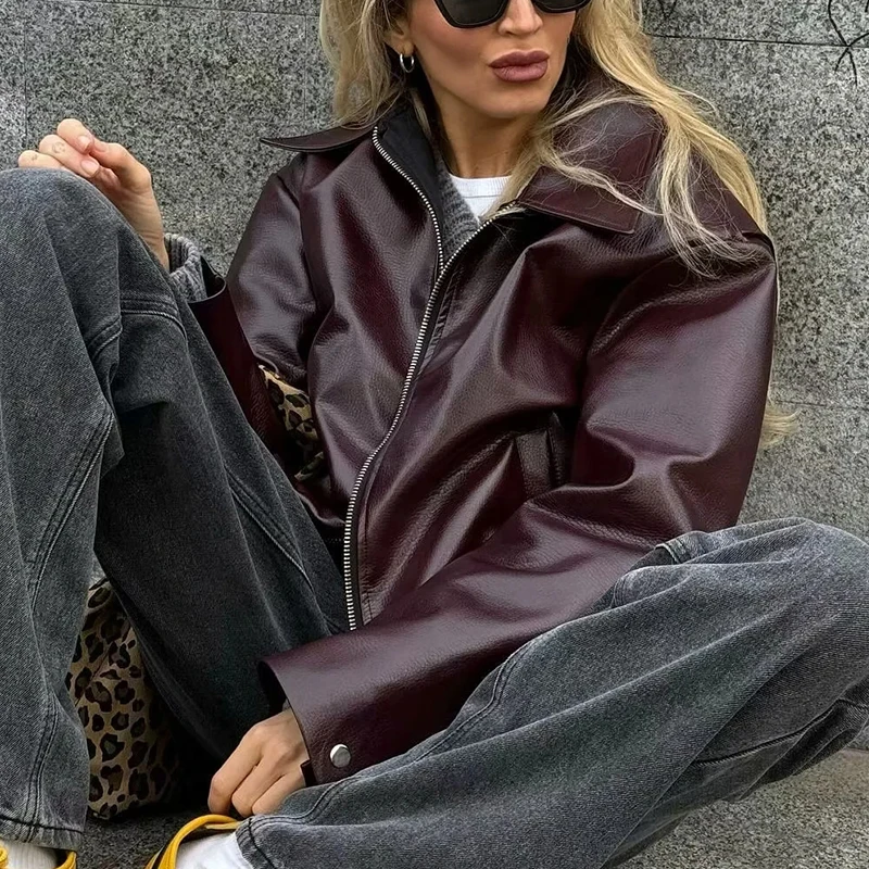 Woman wearing oversized burgundy faux leather jacket with layered necklaces and pinstripe pants.

