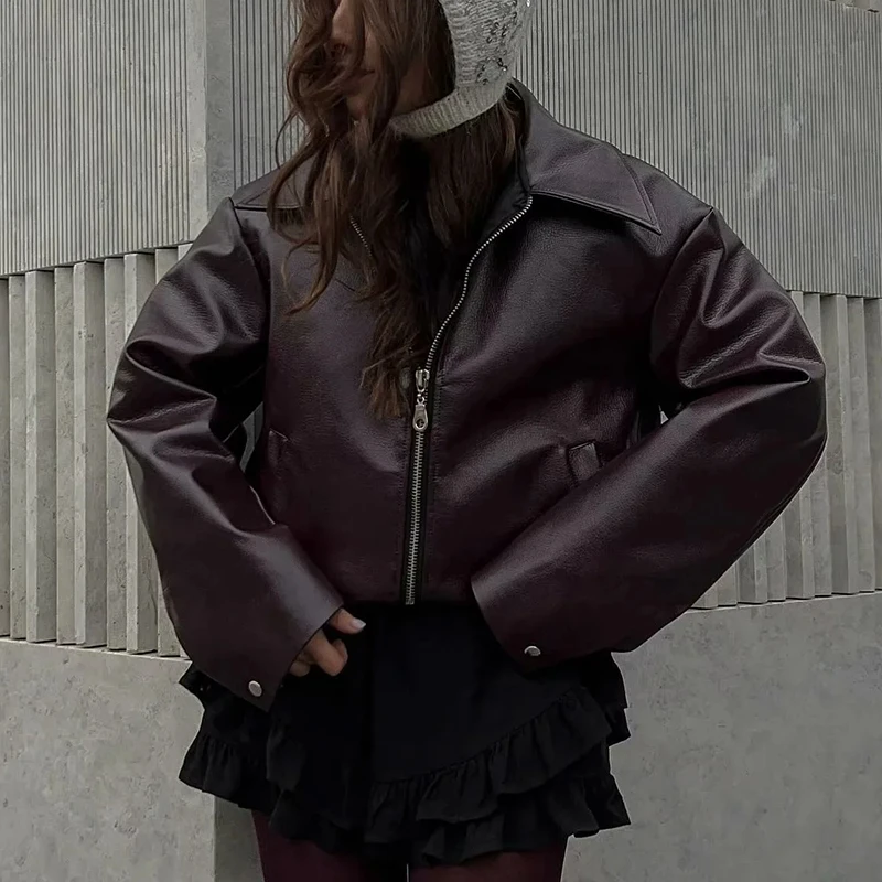 Woman wearing oversized burgundy faux leather jacket with layered necklaces and pinstripe pants.

